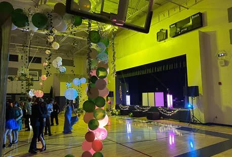 School dance in a gym with balloon arch and lit stage