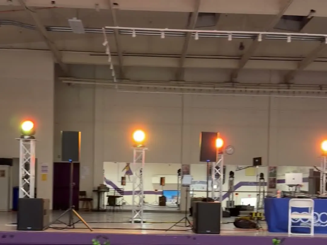 Lighting truss towers with amber moving-head lights beside rented speakers
