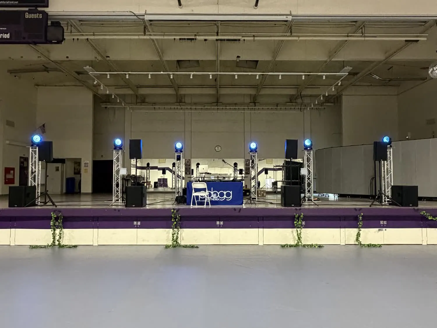 Truss totems with moving-head lights glowing blue across a school stage